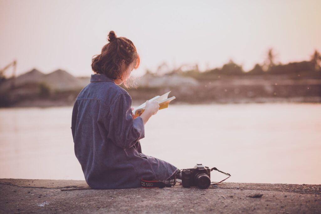 川辺で夕日を見ながら本を読む女性