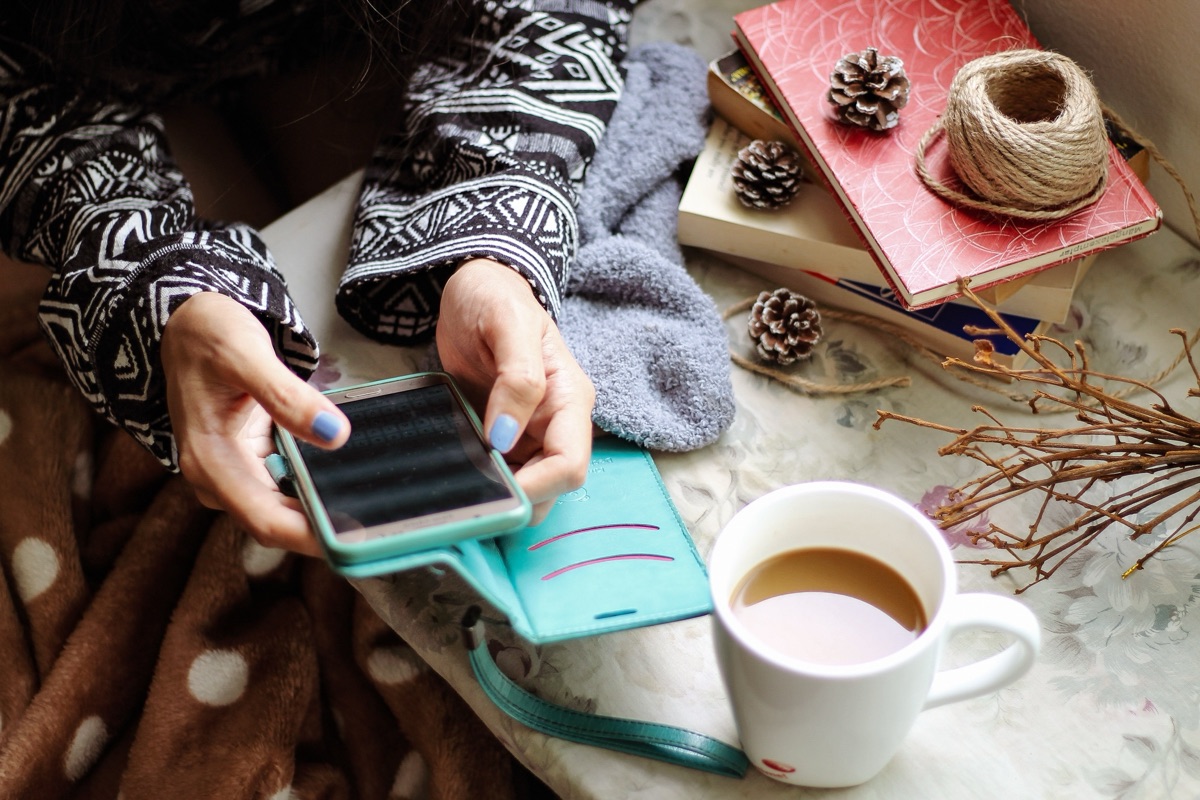 ソファでスマートフォンを操作しながらコーヒーを飲む様子